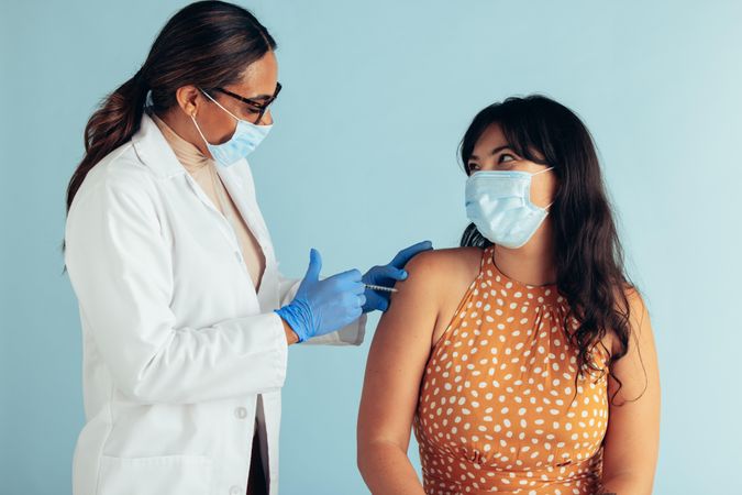Female doctor and woman patient wearing face masks during vaccination