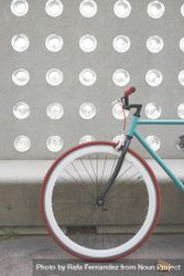 Red and green bike parked in front of patterned cement wall, vertical 5RQ7N0