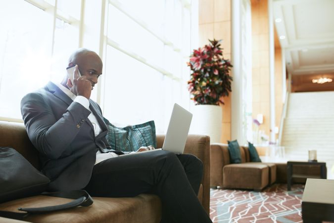 Businessman sitting on sofa working using cell phone and laptop