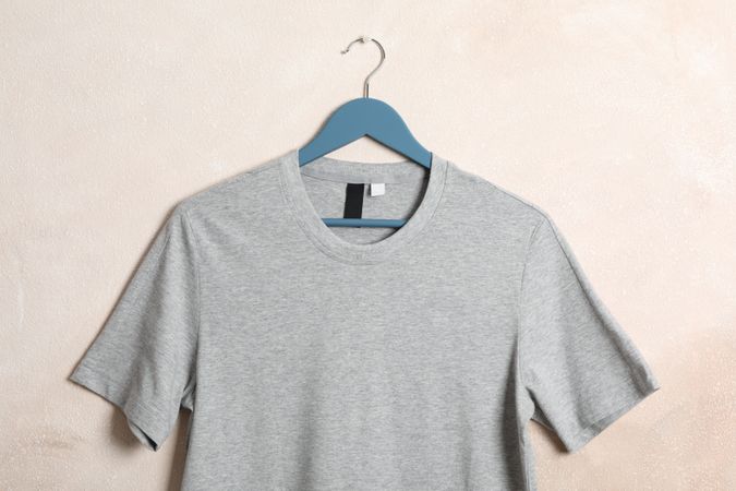 Hanger with blank gray t-shirt on light brown background, space for text