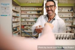 Male pharmacist taking prescription from customer at pharmacy 4NaRm5