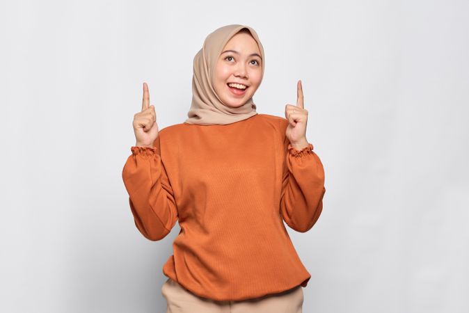Muslim woman in headscarf and orange sweater pointing upwards