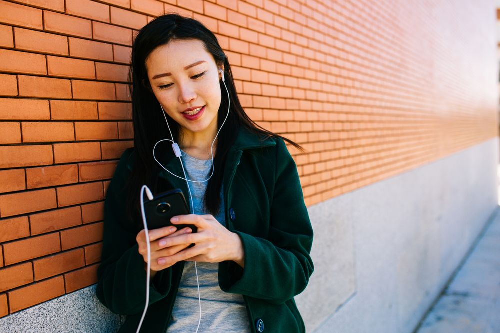 Asian female listening to music near brick wall