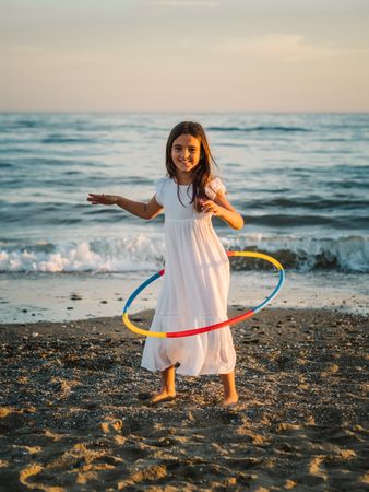 Adorable girl playing with hula hoop ribbon on seaside