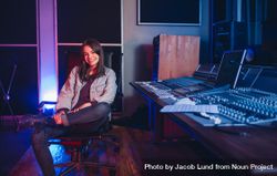 Happy young woman sitting in music studio next to sound board 5wMnLb