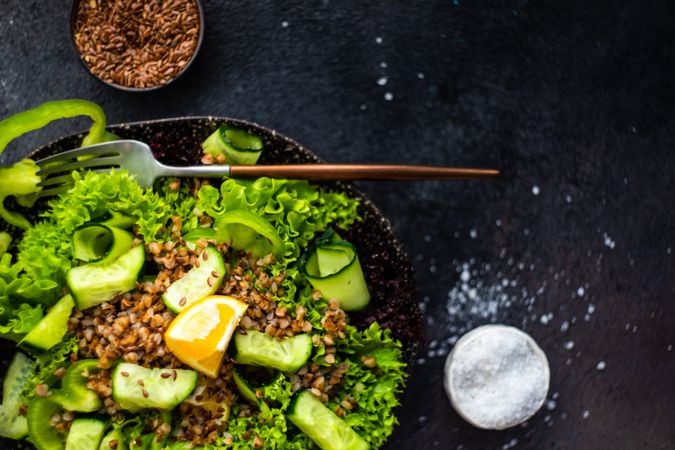 Green fresh salad on concrete background served with flax seed and salt with copy space
