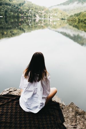 Woman sitting on blanket near lake and mountains