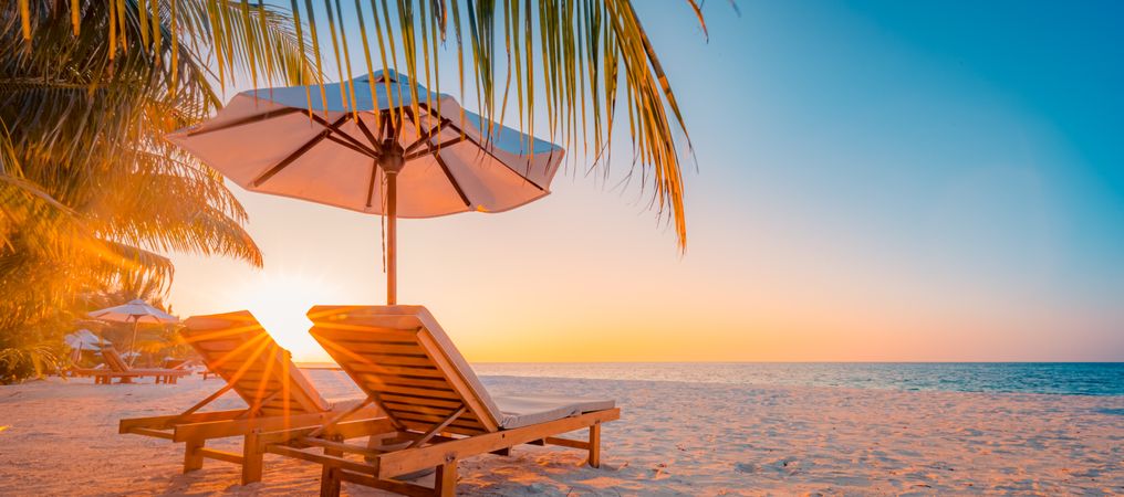 Two lounge chairs on the beach with a sun flare