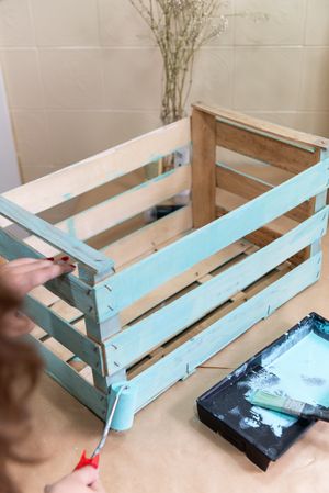 Woman paining wooden box in blue color with roller