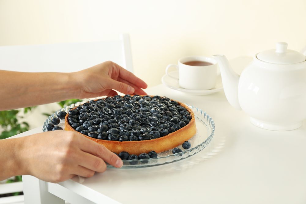 Woman hands hold tasty blueberry pie on table