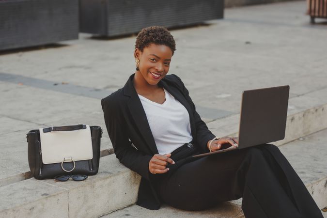Stylish Black woman with laptop on steps near handbag
