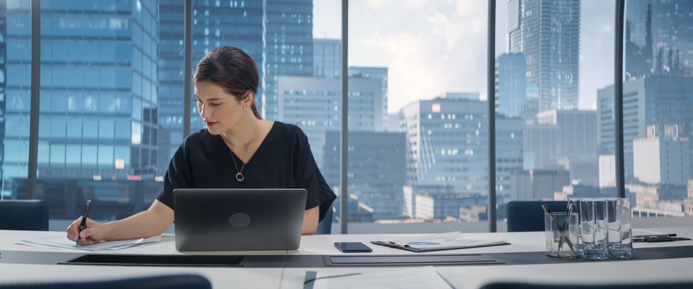 Portrait of Successful Young Businesswoman Sitting at Her Desk Working on Laptop Computer in Big City Office.