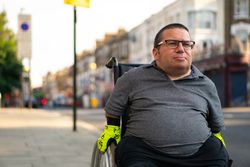 Portrait of man sitting in wheelchair on sidewalk in city 4Me1l4