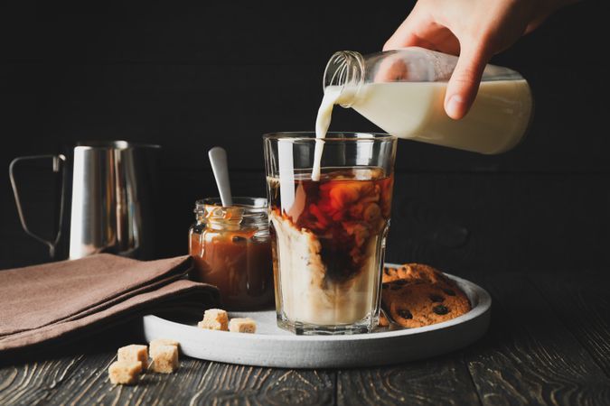 Woman pours a milk in glass of coffee. Composition with ice coffee