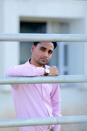Young man in pink shirt standing beside railing outdoor