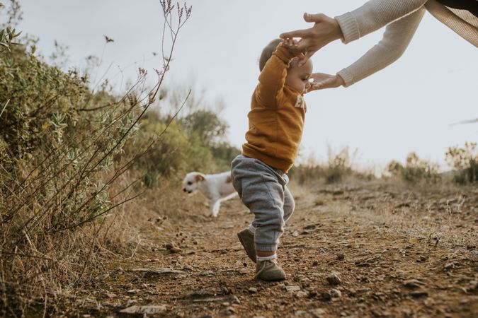 Baby boy standing up with the help of his mother on a walking trail