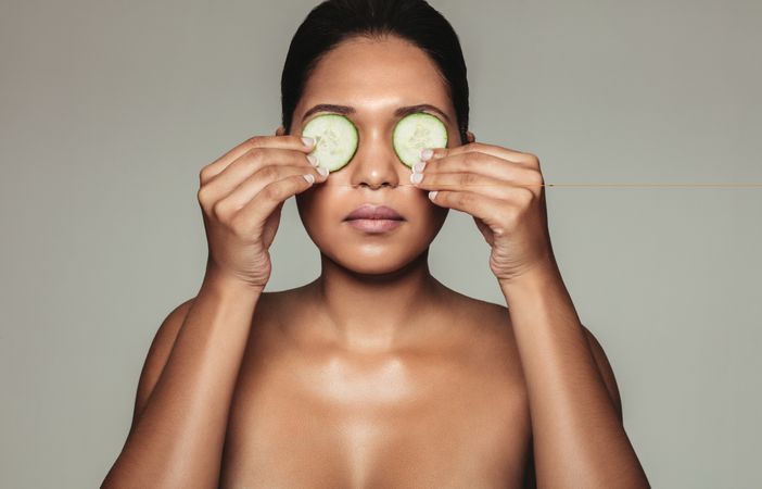 Female with clean skin holding cucumbers to her eyes