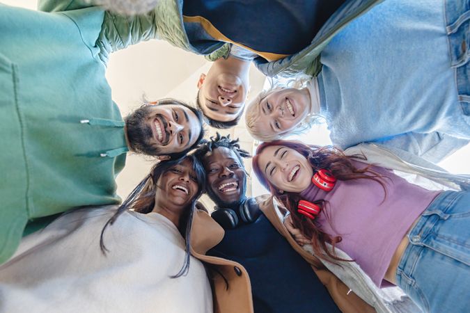 View of a diverse group of joyous friends forming a circle, looking down and smiling