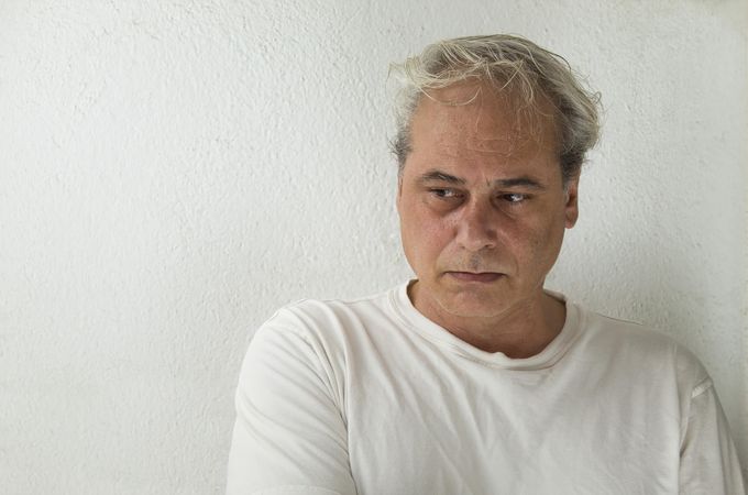 Portrait of middle aged man in light shirt looking away and thinking against light wall