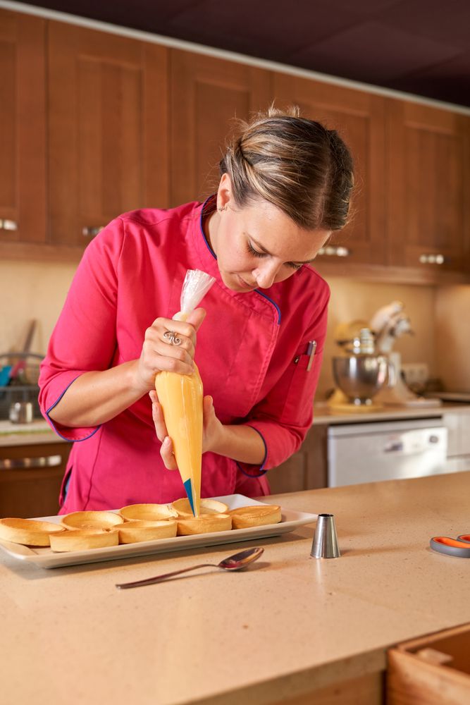 Female pastry chef making peaks of cream on tarts