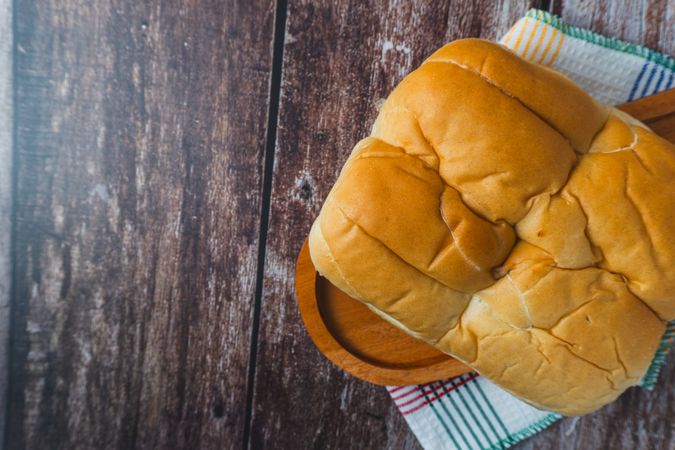 A loaf of bread served on a wooden plate placed on a rustic wooden surface