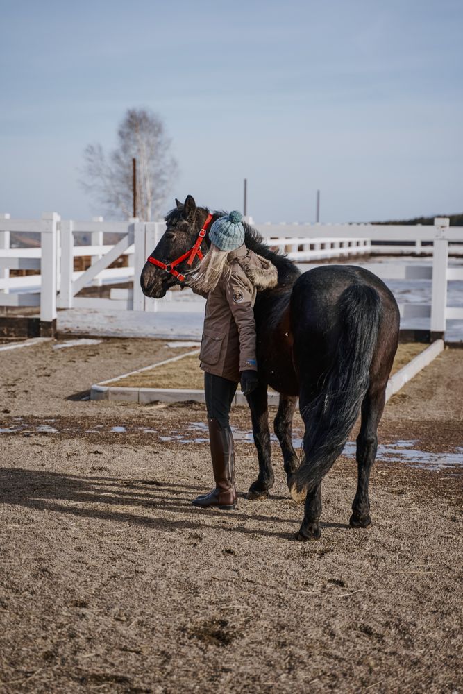 Warm dressed woman with brown horse by hay