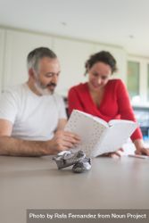 Couple looking reminiscently through book in kitchen with baby shoes in foreground 48wak5