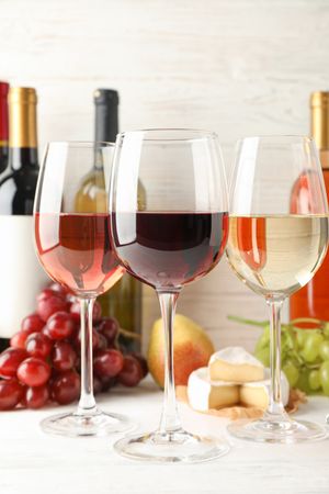 Fruits, cheese, bottles and glasses with different wine on light background, space for text
