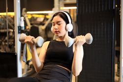 Asian Sport Woman Sit and Stay in Position of Exercise with Hold Dumbbells in Fitness Gym.