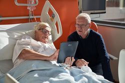Older woman lying on medical bed and sharing tablet with husba