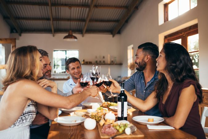 Cheerful friends toasting red wine at dinning table during dinner party