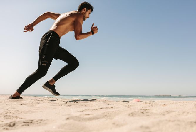 Physically fit man working on his running time at a beach