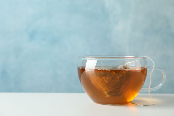 Cup of tea with tea bag on blank background, space for text