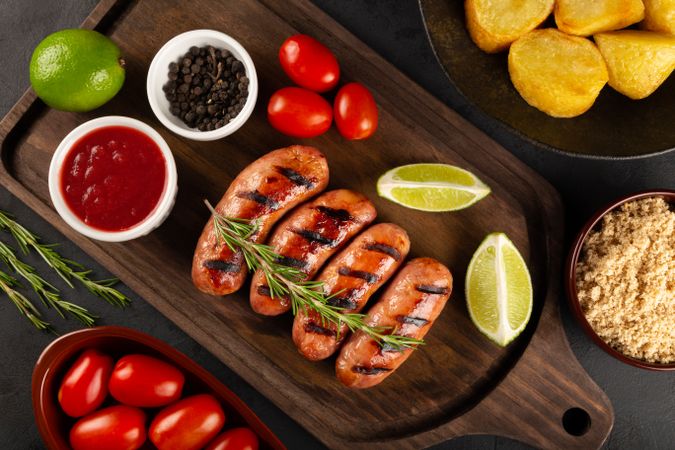 Top view of grilled sausages with condiments, sides and lime slices