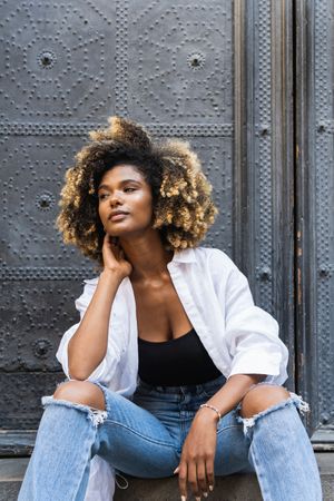 Stylish Black woman sitting on concrete steps near gates