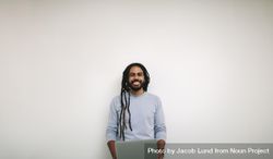 Smiling professional with dreadlocks standing against a light wall bxG2r4
