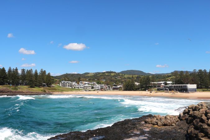 Beautiful coastal view of turquoise waves crashing against rocks near a sandy beach on a sunny day