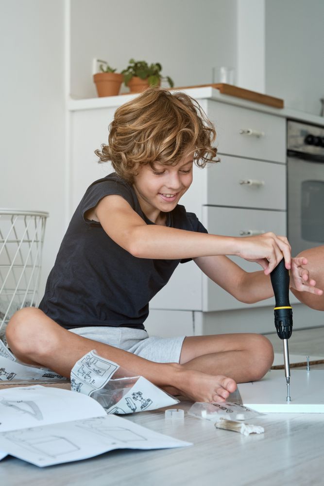 Cheerful boy using screwdriver during furniture assembly