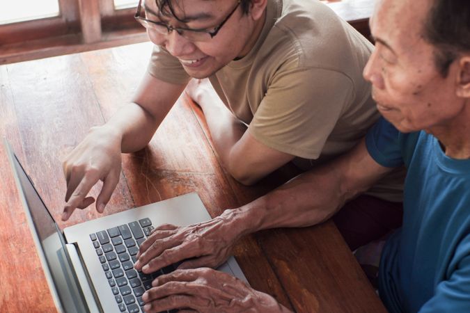 Happy adult son teaching older father using laptop