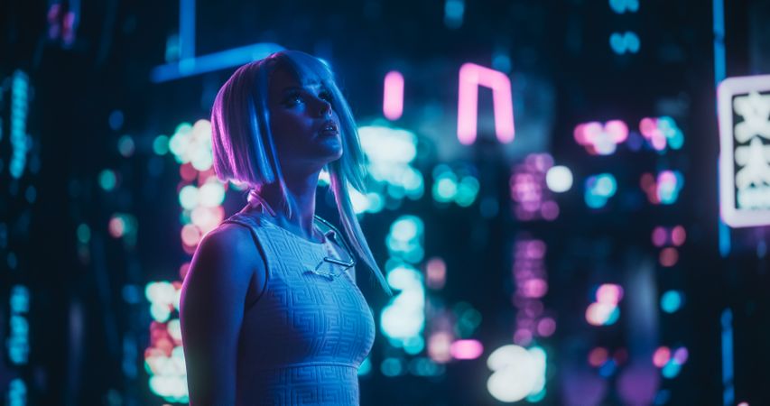 Creative Young Female Standing in a Sci-Fi Cyberpunk City with Neon Lights, Dystopian Colorful Urban Environment. Cosplay Model with Blue Hair Excited About Technological Surroundings