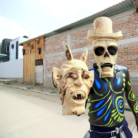 Man with skull face mask holding a mask standing outdoor in a village in Oaxaca, Mexico