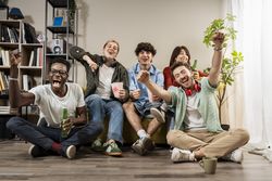Group of diverse young friends cheering and eating popcorn together during a fun living room movie night