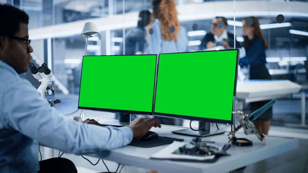 Software Developer Working on Computer with Green Screen Mock Up Display.