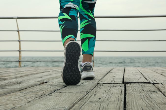 Female legs in bright leggings and sneakers on wooden floor outdoors, close up