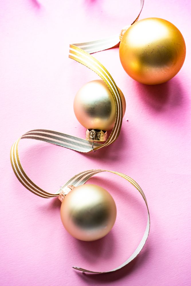 Gold Christmas baubles on pink background with ribbon