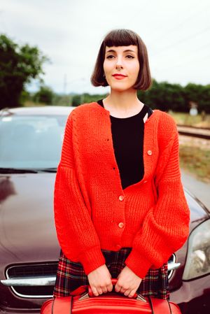 Smiling woman in red with suitcase nearby car