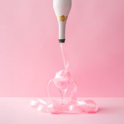 Champagne bottle with pink party ribbon on pink background