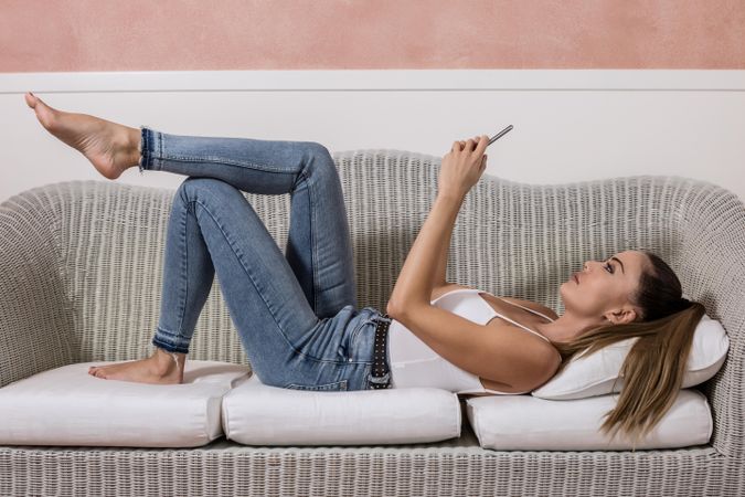Side view of woman laying on sofa using smartphone