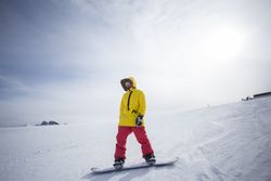 Man in yellow parka on top of mountain with snowboard