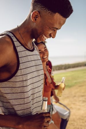 Smiling Black man holding beer walking with friends outdoors on summer day
